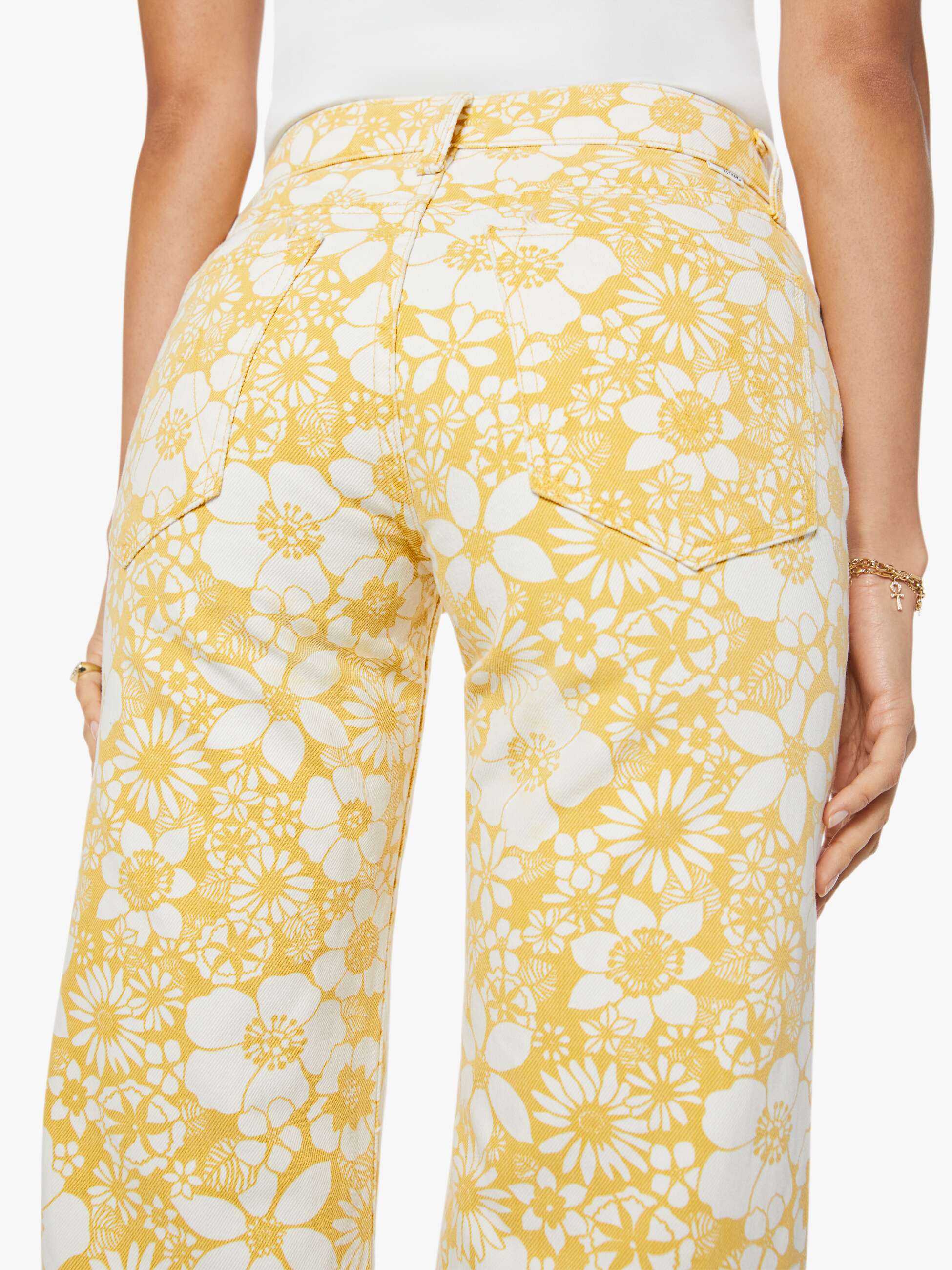 Woman wearing a white top and yellow floral pants on a white background