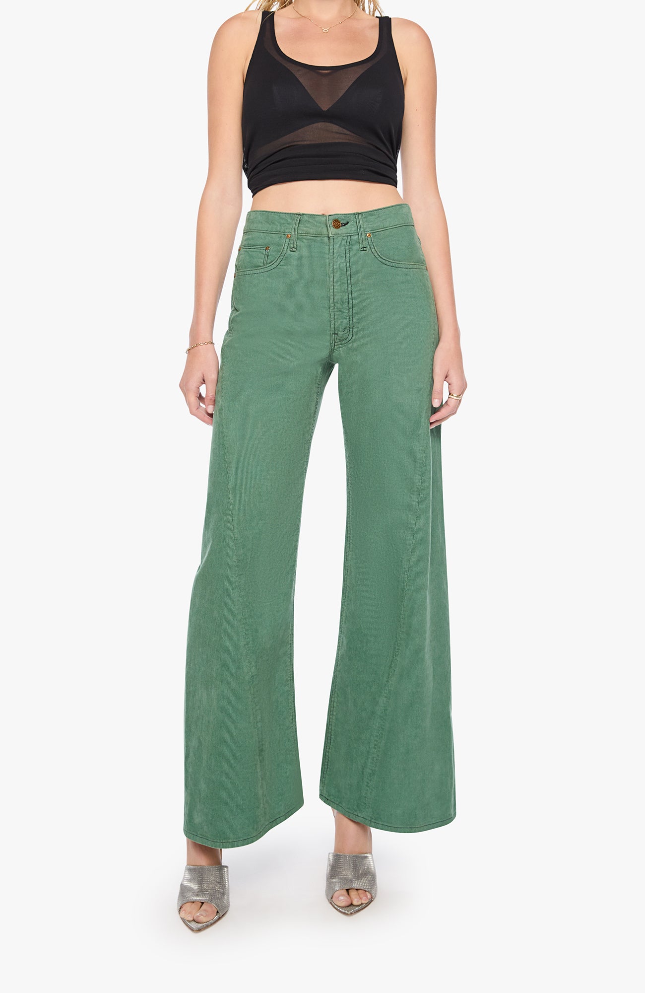 A model wearing a pair of sage green wide-leg cropped jeans with a black mesh crop top and metallic silver heels, shown against a plain white studio background.