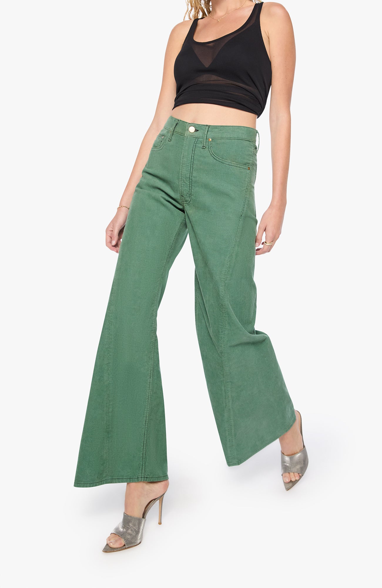 A model wearing a pair of sage green wide-leg jeans with a black crop top and metallic silver high heels, shown from the waist down against a plain white background.