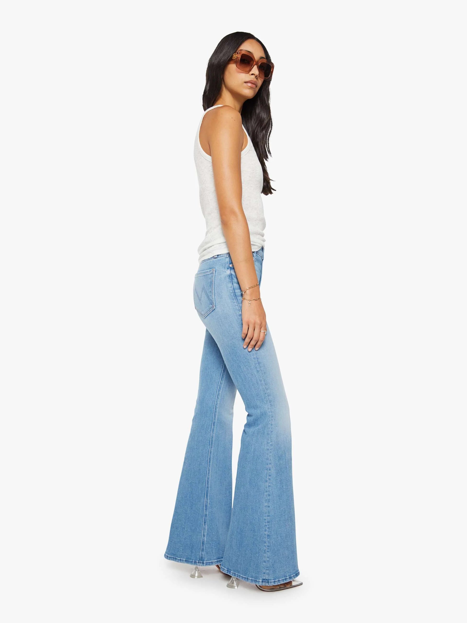 Woman wearing light blue flared jeans and a white top on a white background