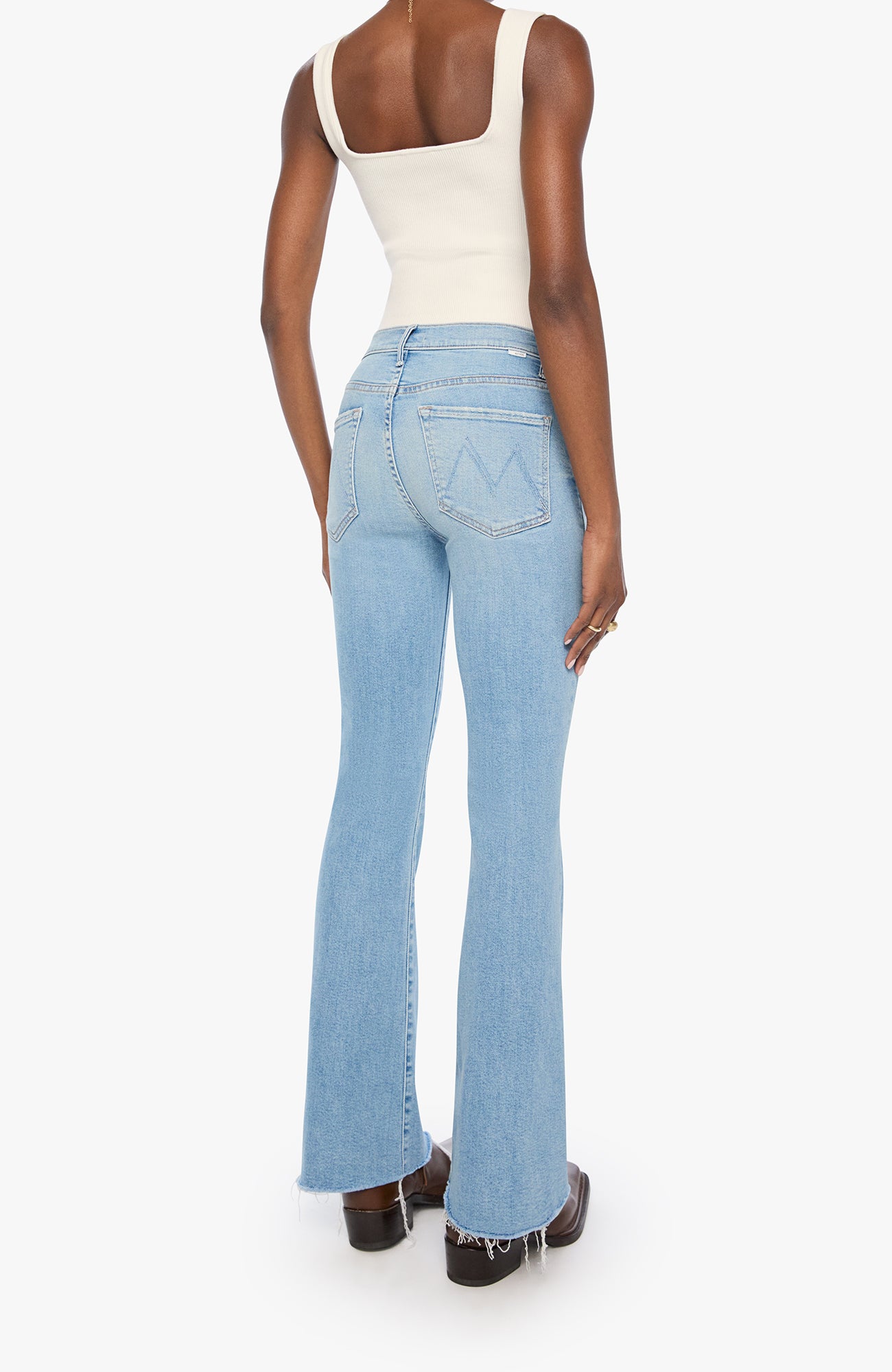 A model shown from the back wearing light-wash blue flare jeans, a cream tank top, and brown platform shoes against a plain white background.