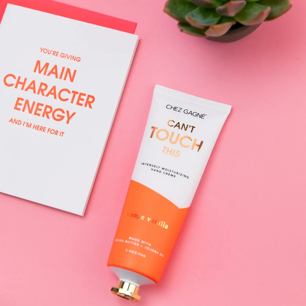 Hand cream tube labeled 'Can't Touch This' by Chez Gagne on a pink background with a motivational card.