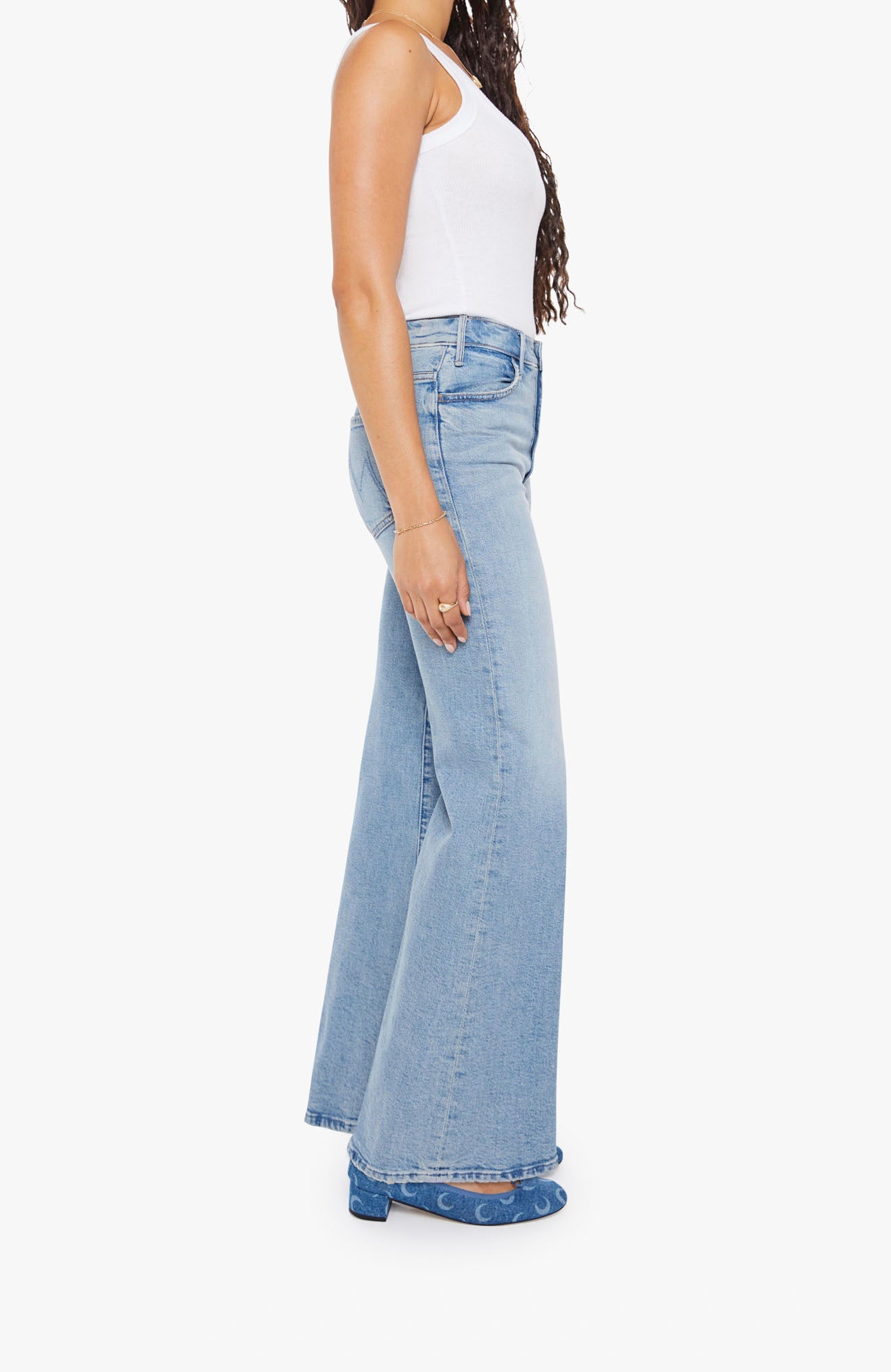 Woman wearing light blue flared jeans and a white top on a white background