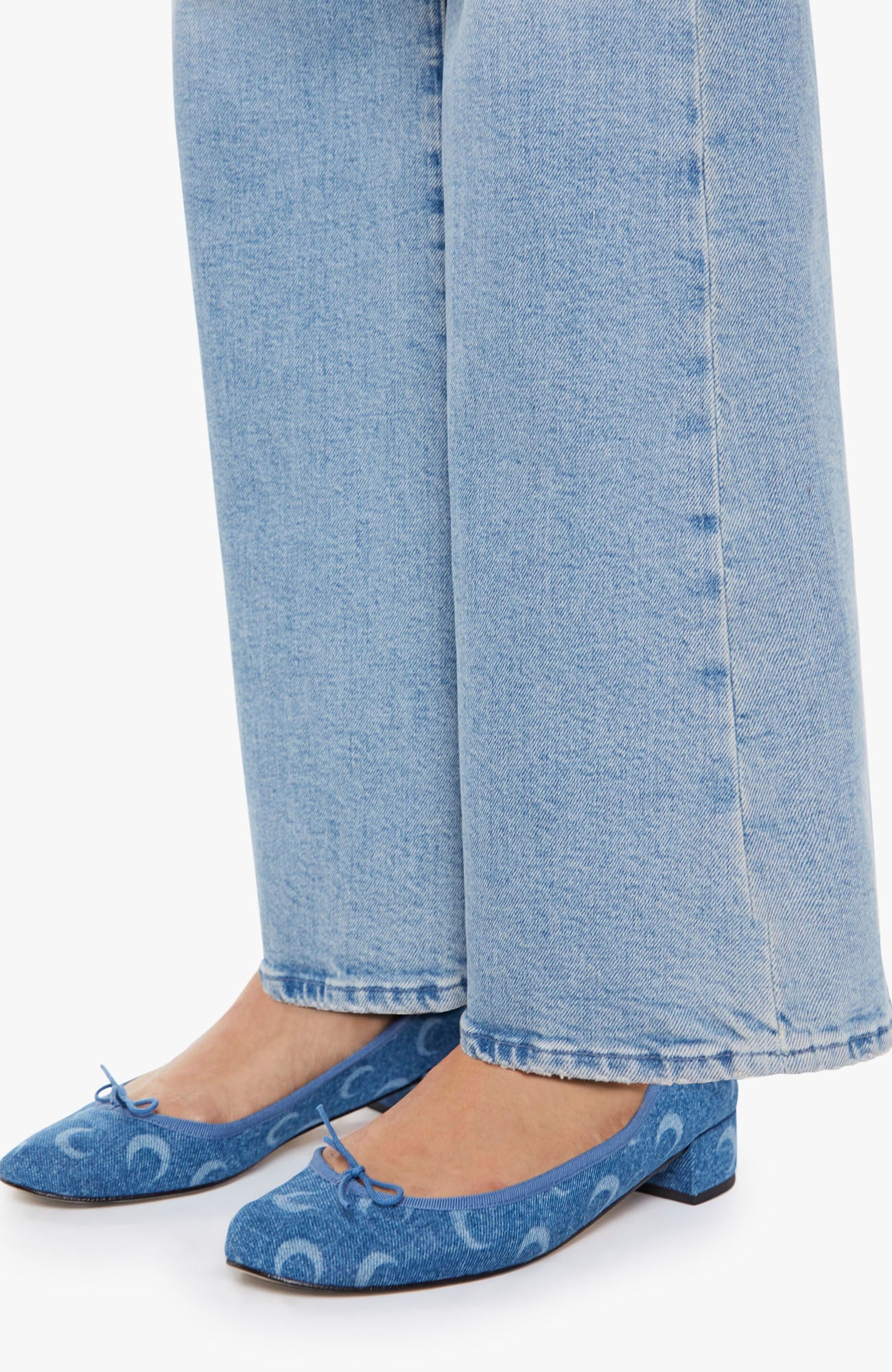 Person wearing blue denim shoes with white patterns and light blue jeans on a white background