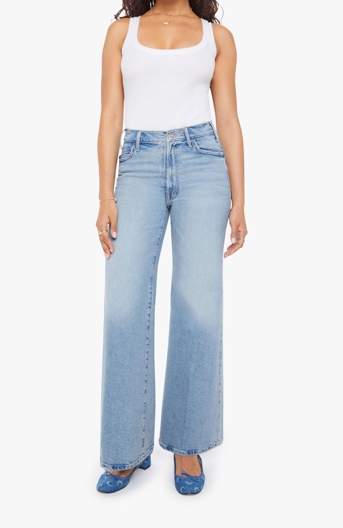 Woman wearing light blue flared jeans and a white tank top on a white background