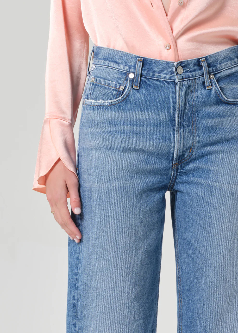 Person wearing light blue jeans and a pink shirt against a gray background