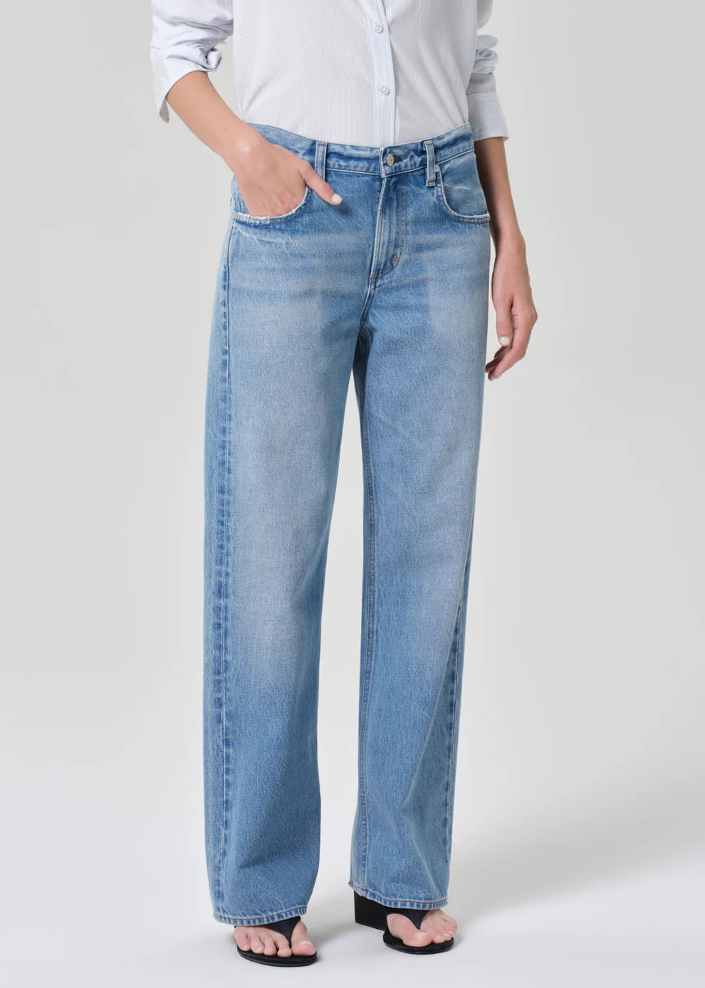Person wearing light blue jeans and a white shirt on a plain background