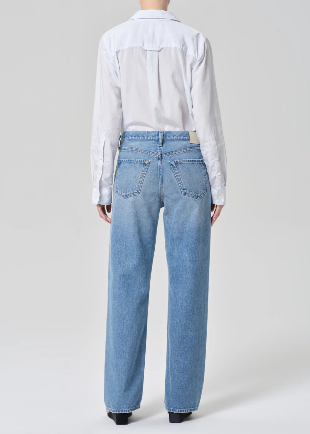 Person wearing a white shirt and light blue jeans on a plain background