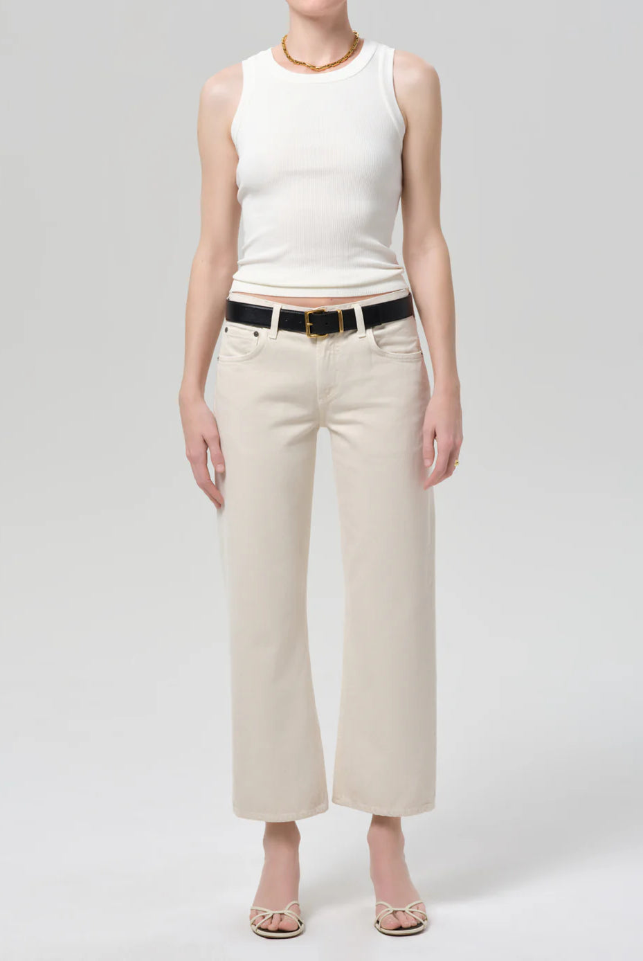 Person wearing a white sleeveless top and beige pants on a plain background