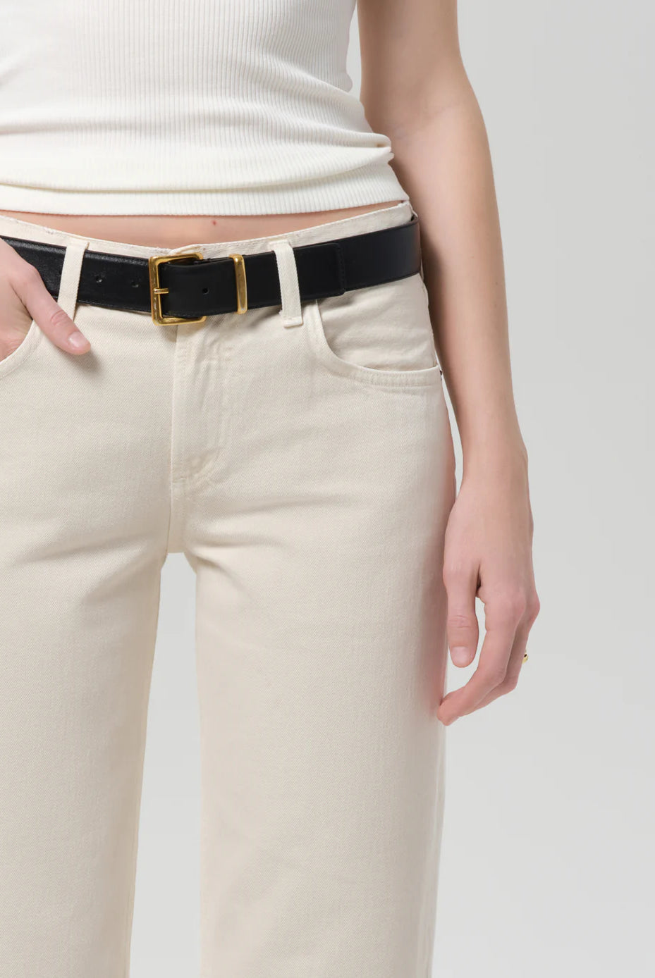 Person wearing a black belt with a gold buckle on beige pants against a white background