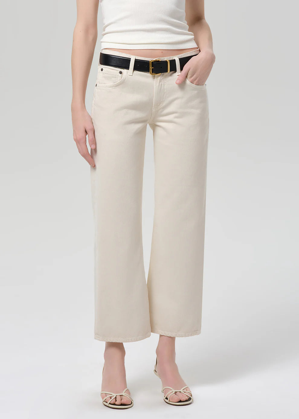Person wearing beige wide-leg pants with a white top on a plain background