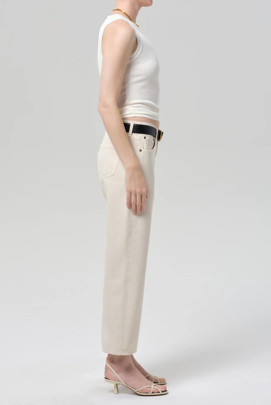 Person wearing a white sleeveless top and beige pants on a plain background