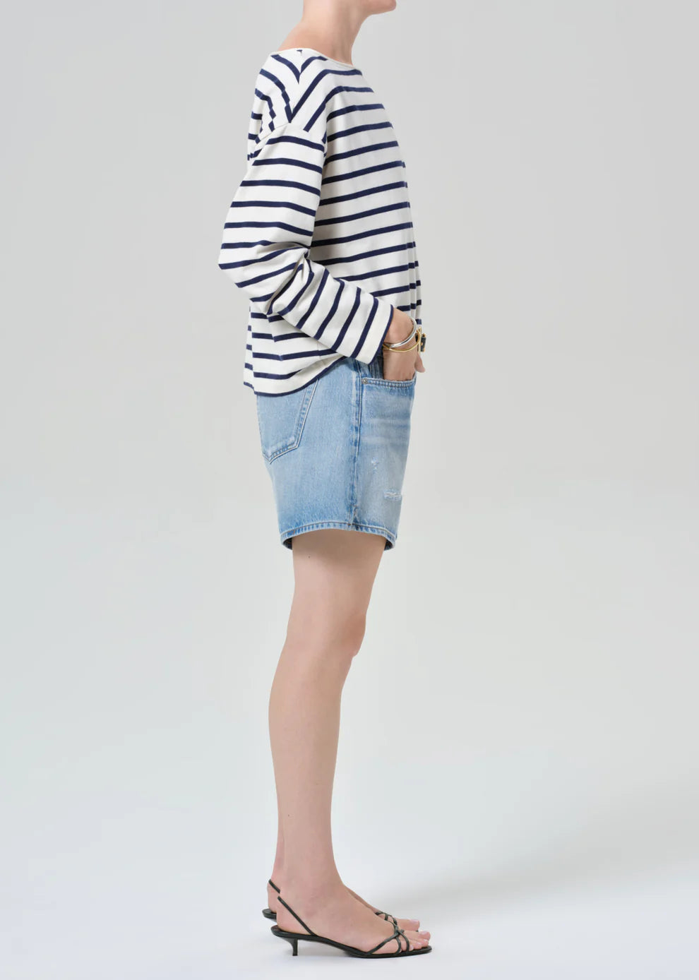 Person wearing a striped sweater and denim shorts on a plain background