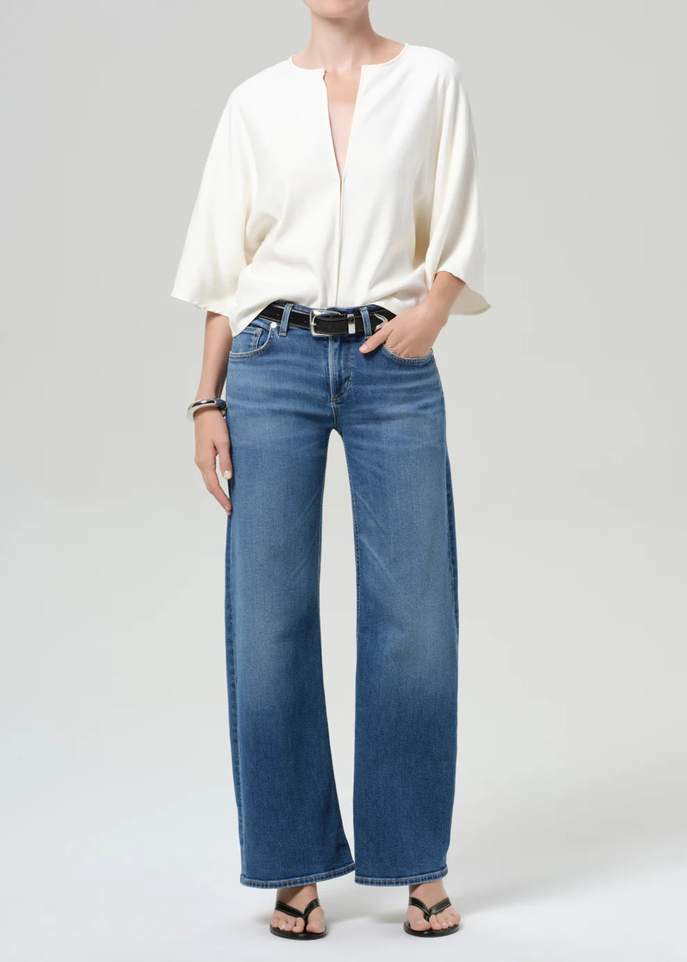 Person wearing a white blouse and blue jeans on a plain background