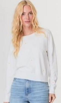 Woman wearing a white sweater and light blue jeans against a plain background