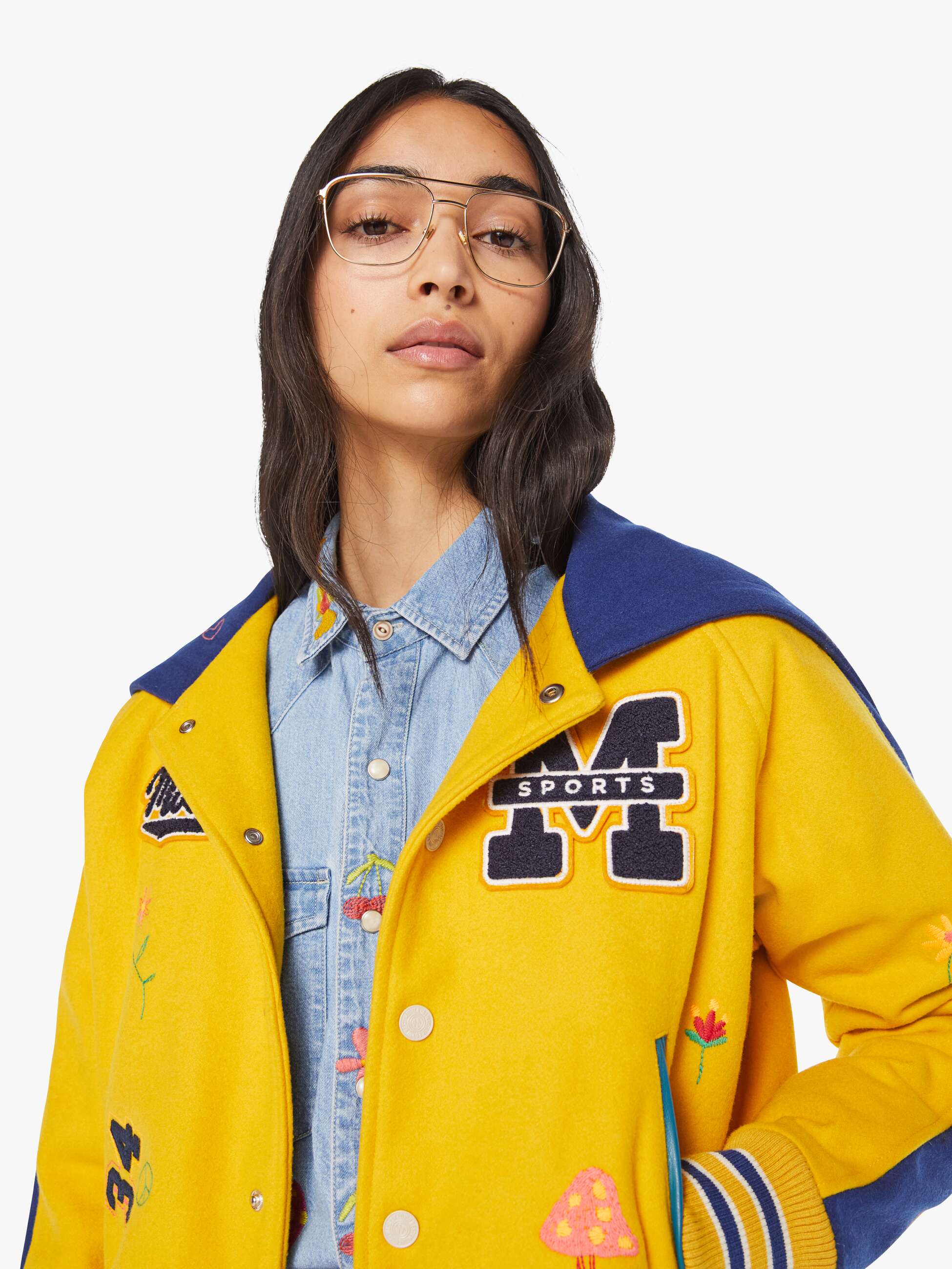 Person wearing a yellow varsity jacket with patches on a white background