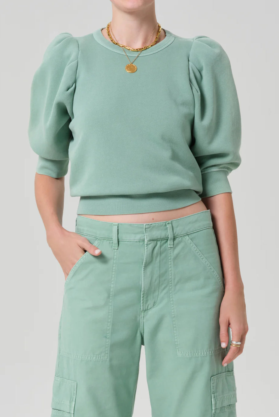 Person wearing a green sweater and pants on a light gray background