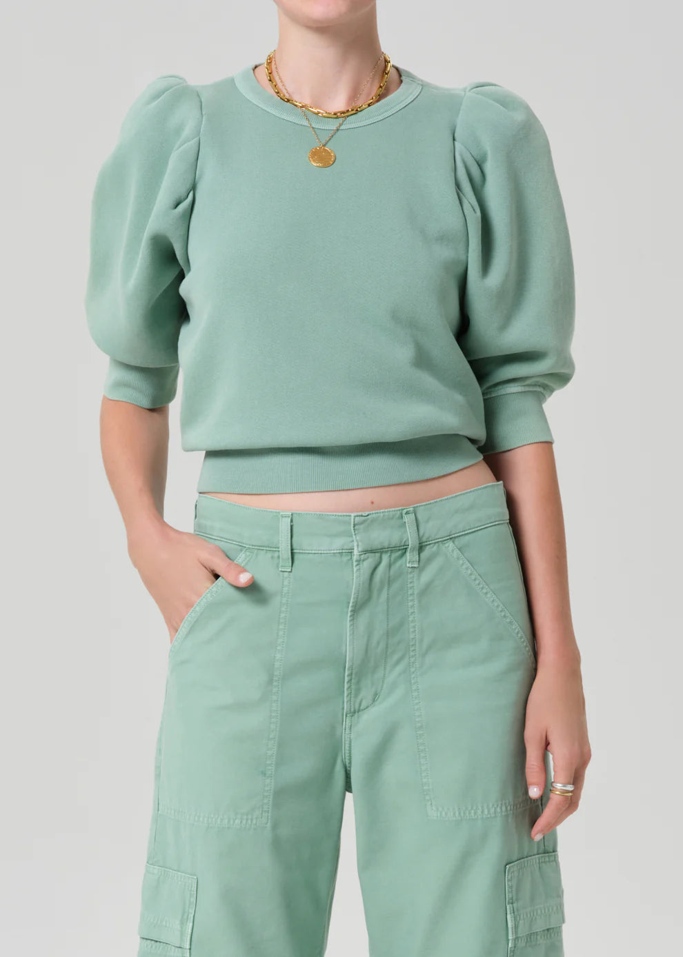 Person wearing a green sweater and pants on a light gray background