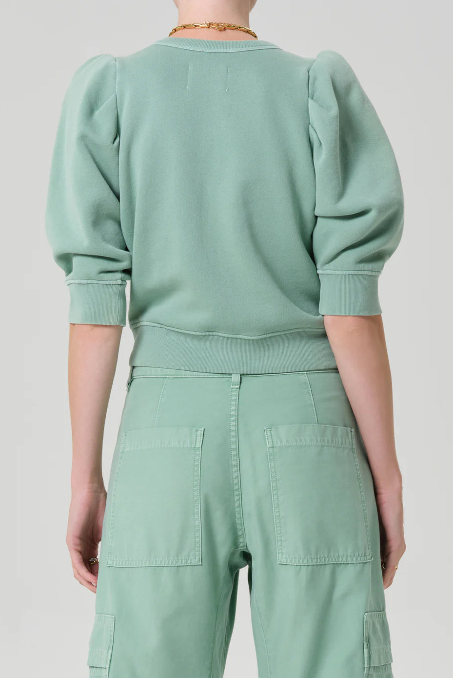 Person wearing a mint green outfit with a matching sweater and pants on a light gray background