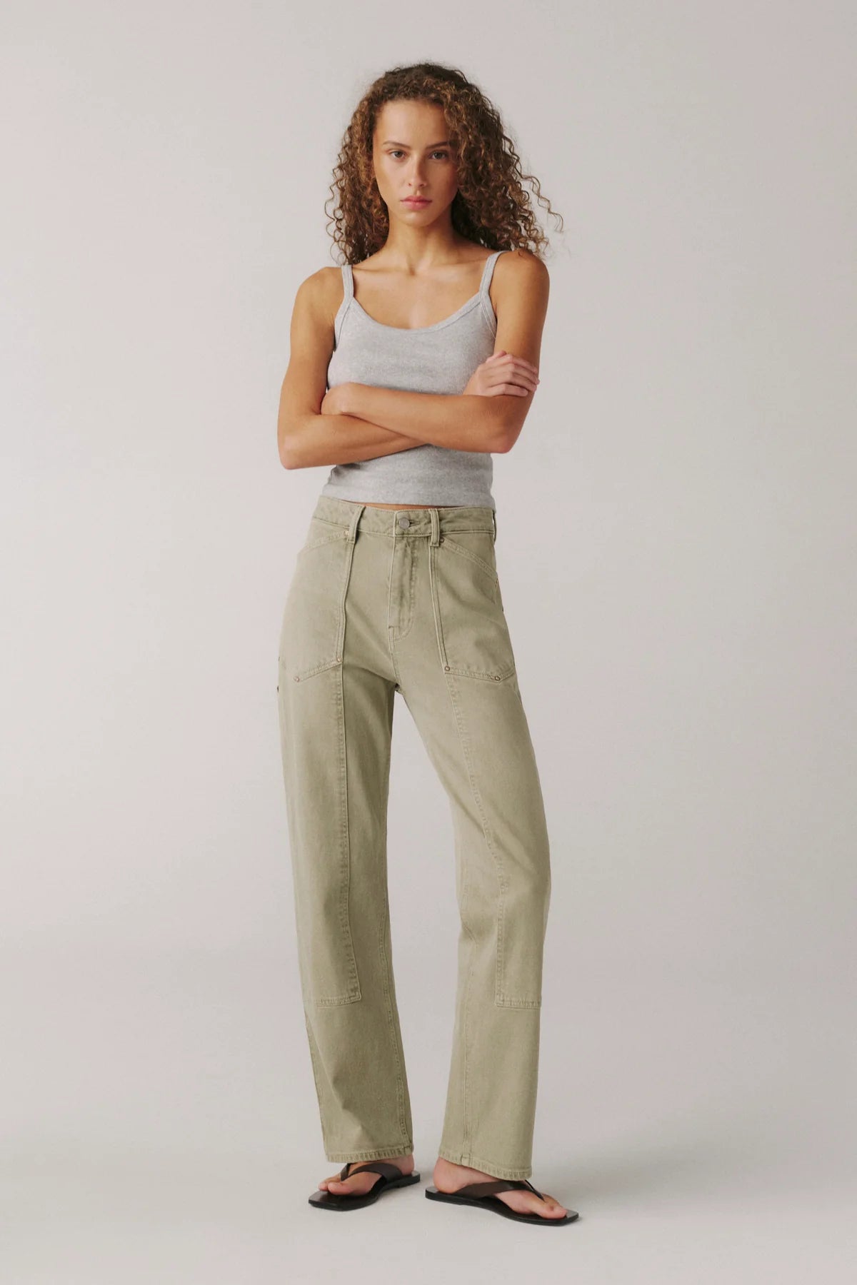Woman wearing a gray tank top and beige pants on a plain background