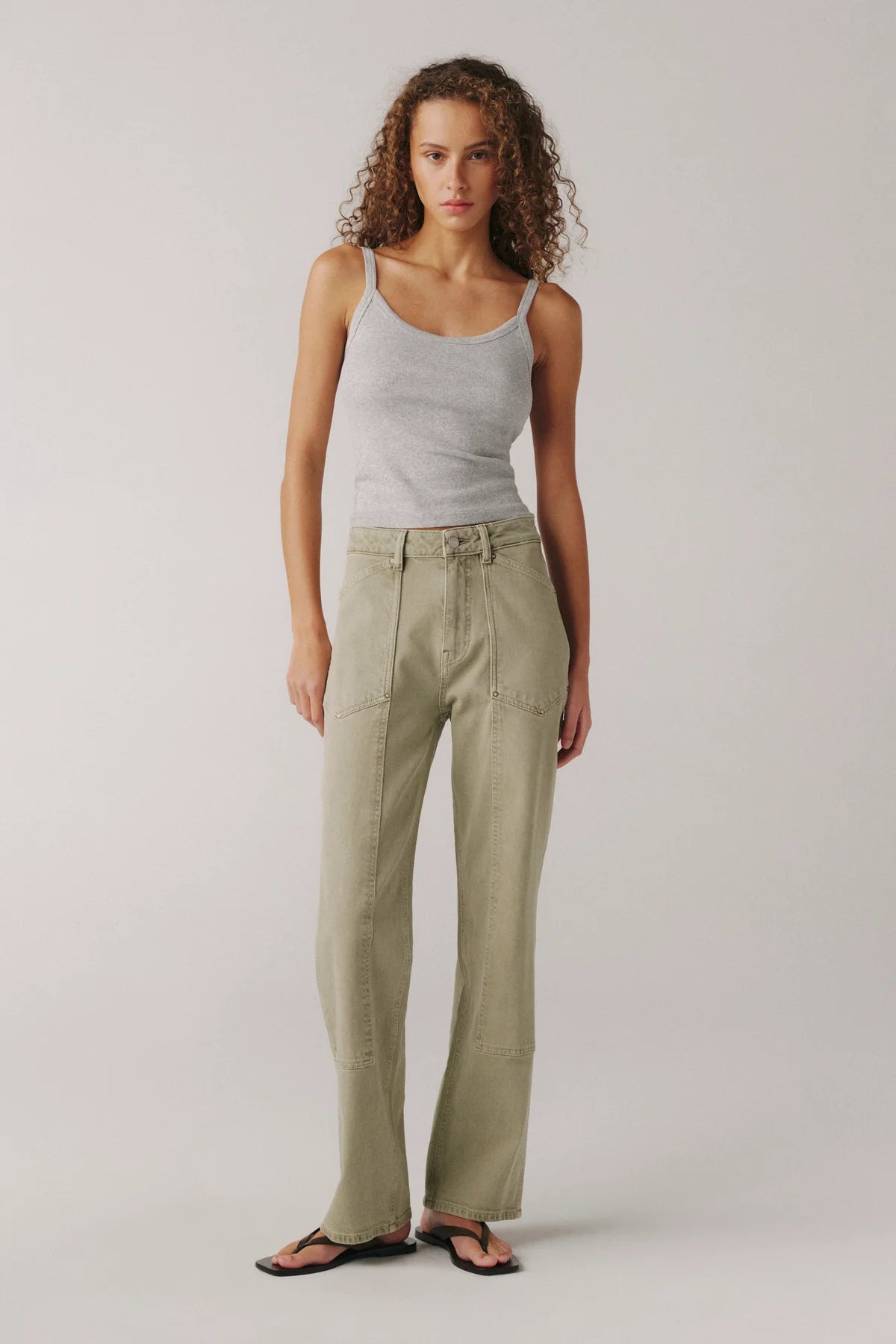 Woman wearing a light gray tank top and beige pants on a plain background