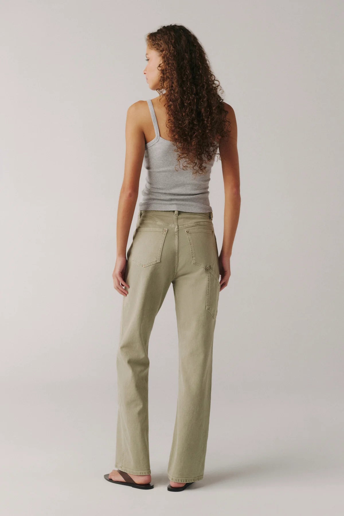 Woman wearing a gray tank top and beige pants on a plain background