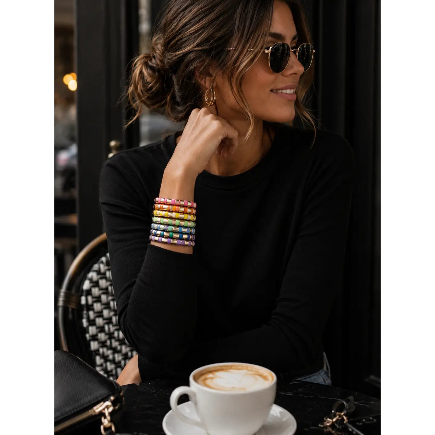 Woman sitting at a table with a cup of coffee, wearing colorful bracelets.