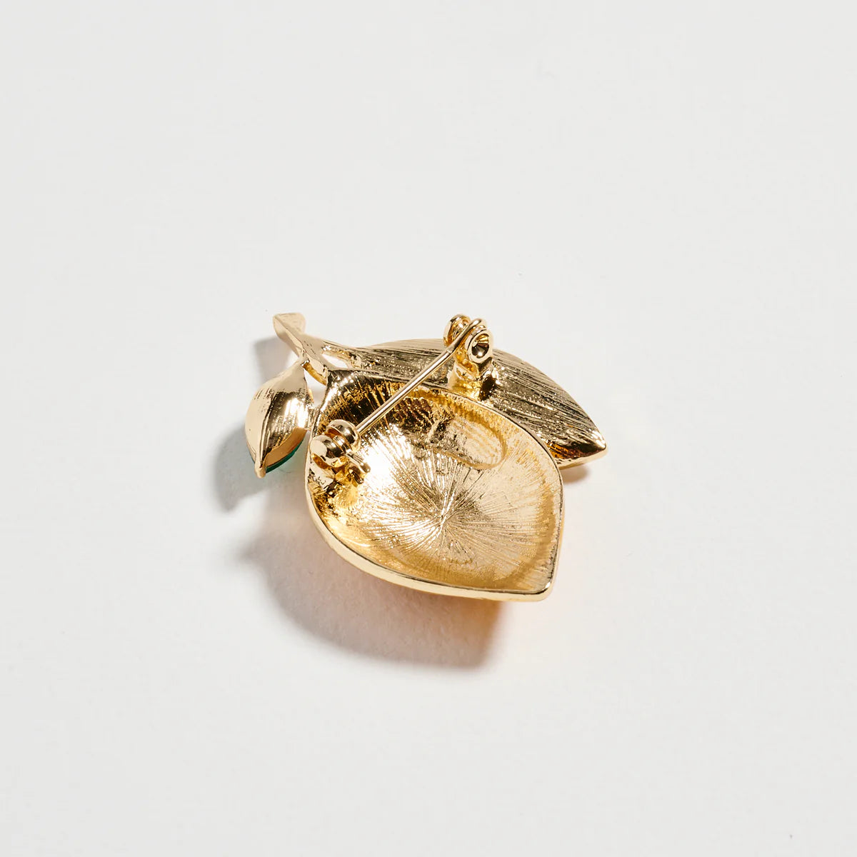 Gold leaf-shaped brooch on a light gray background