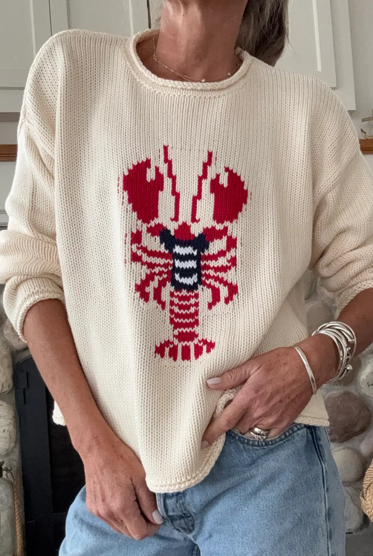 Person wearing a cream sweater with a red and blue lobster design, standing in a casual setting.