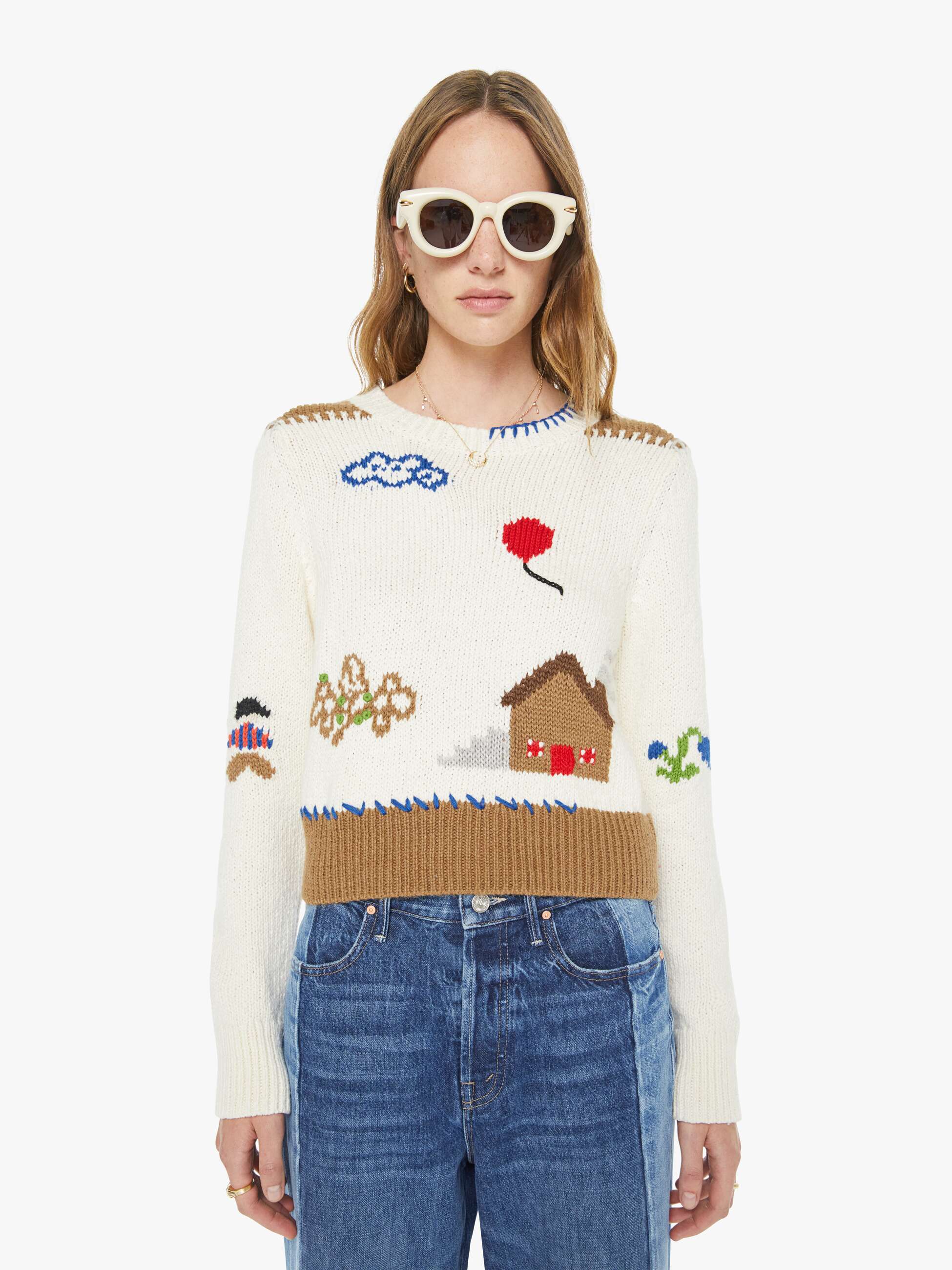 Person wearing a colorful sweater with various designs and blue jeans on a white background
