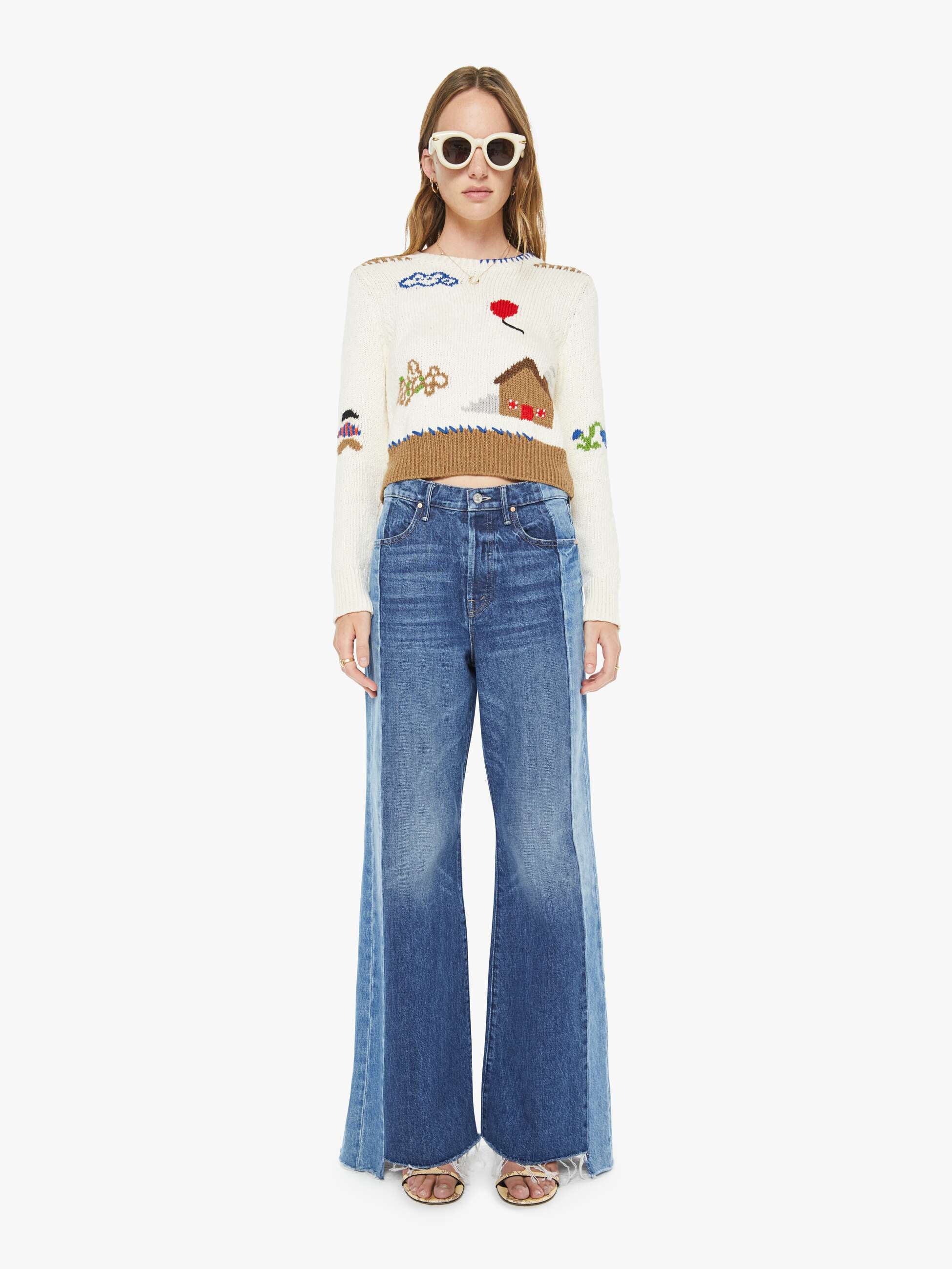 Woman wearing a sweater with embroidered designs and blue jeans on a white background