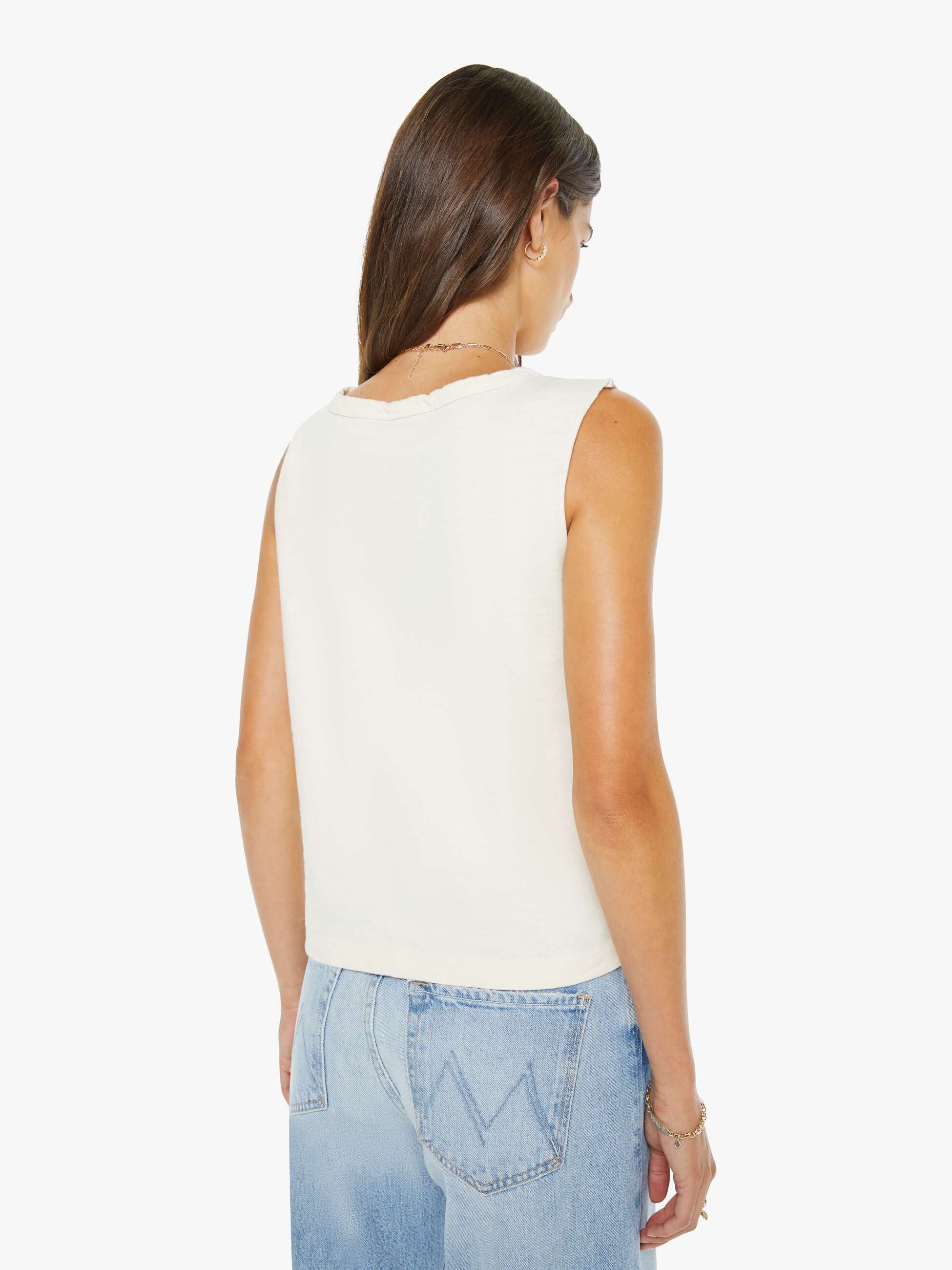 Woman wearing a white sleeveless top and light blue jeans on a white background