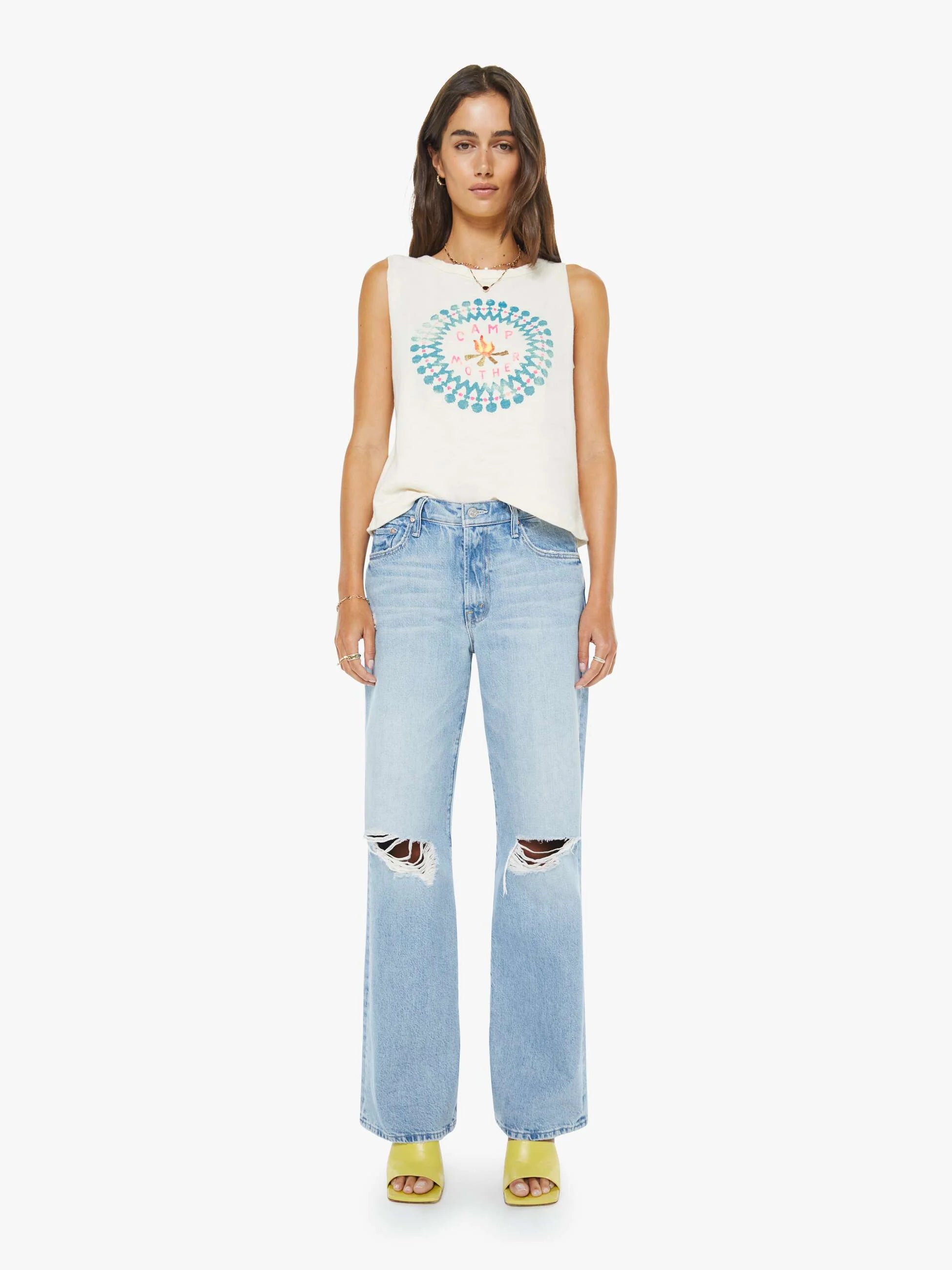 Woman wearing a sleeveless top with a circular design and light blue jeans on a white background