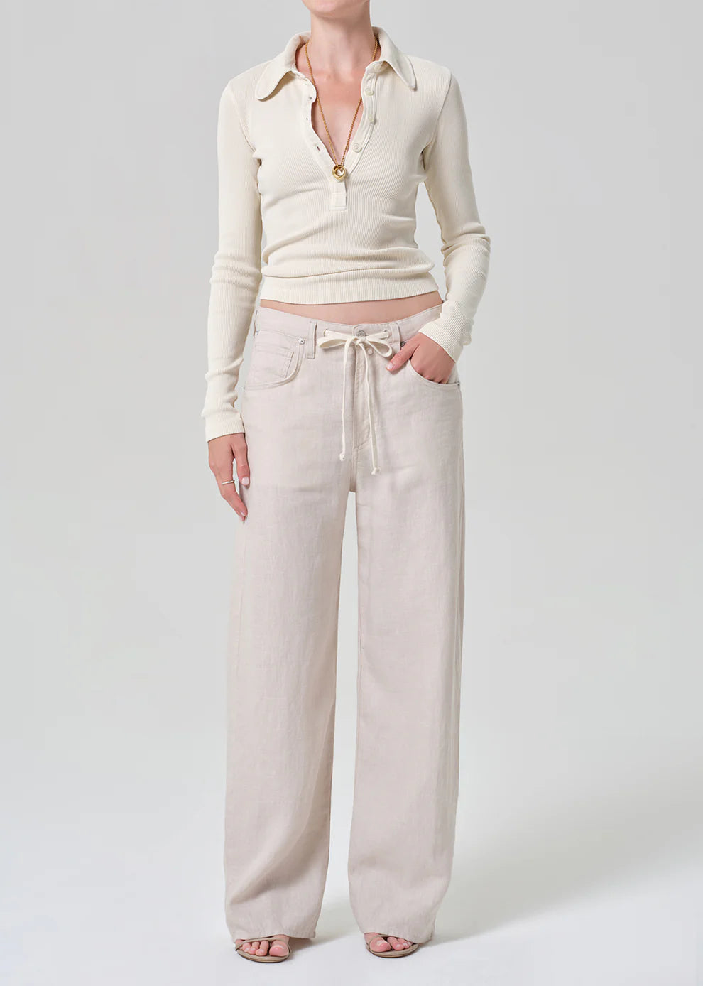Person wearing a cream-colored outfit with a cardigan and wide-leg pants on a white background