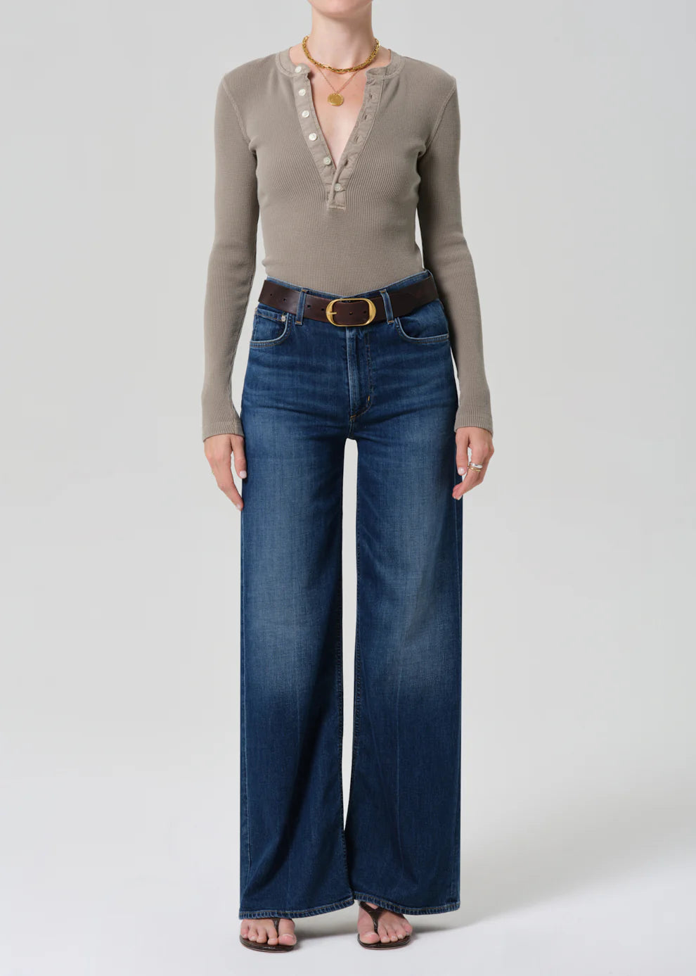 Person wearing a beige long-sleeve top and blue jeans on a white background