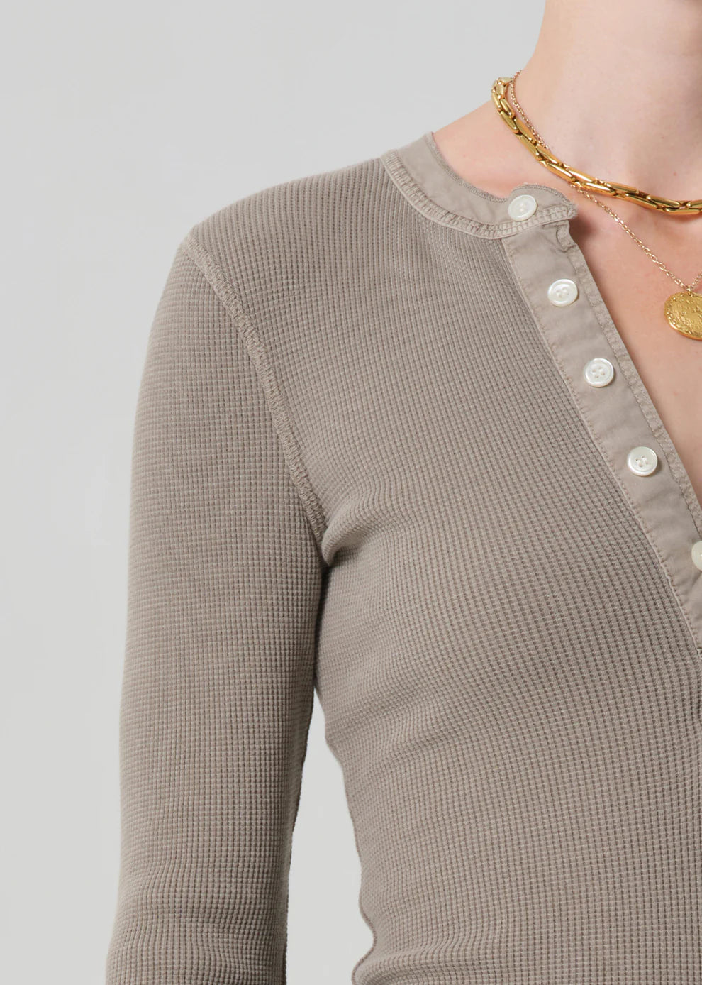 Close-up of a person wearing a brown textured long-sleeve top with a plain background
