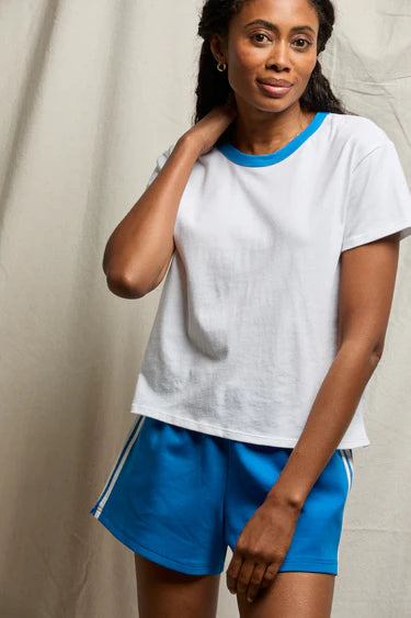 Woman wearing a white t-shirt with blue trim and blue shorts against a neutral background