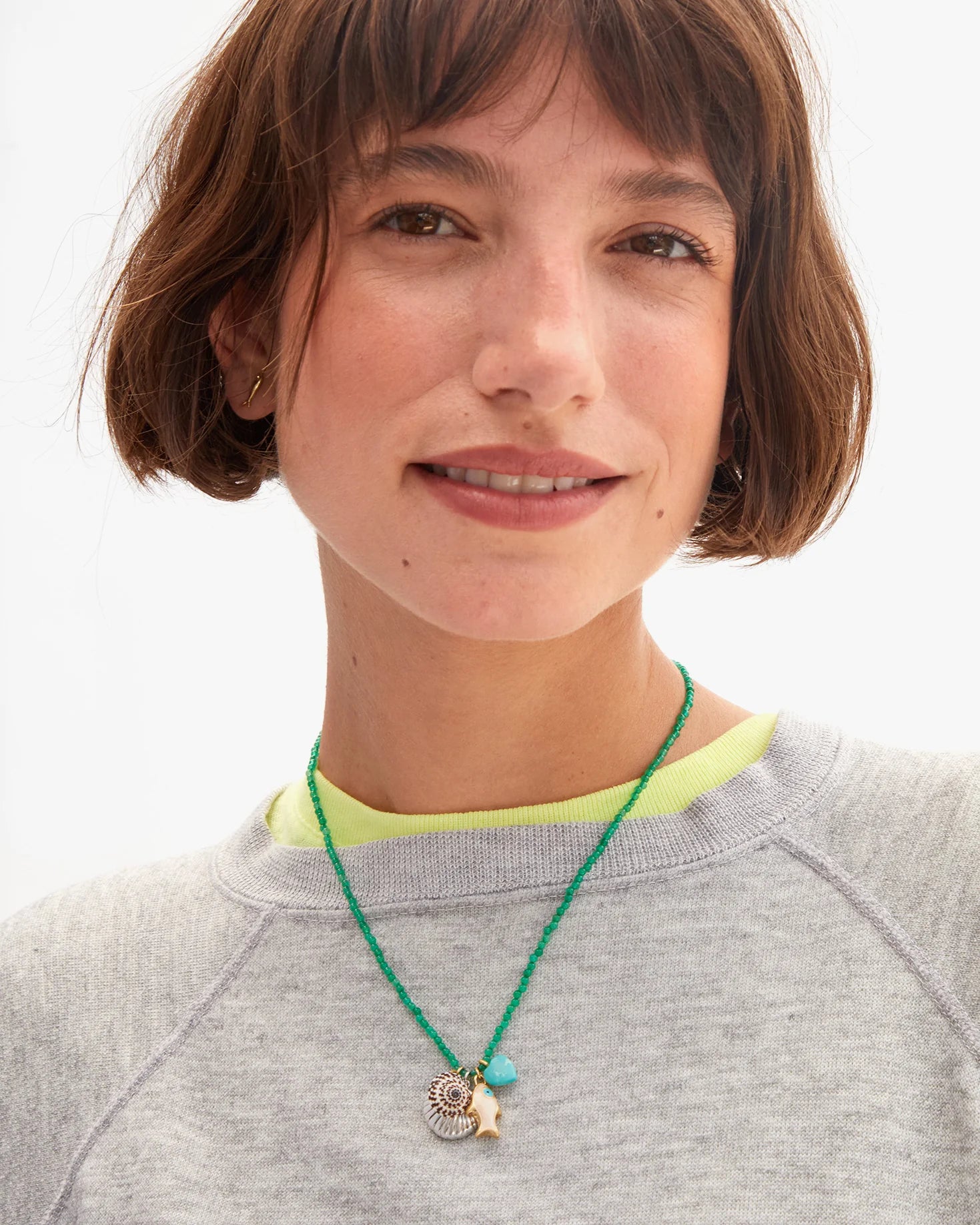 Person wearing a green necklace with charms on a plain background