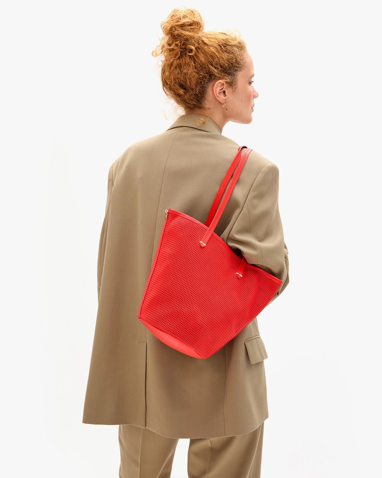 Person wearing a beige coat with a red bag on a white background
