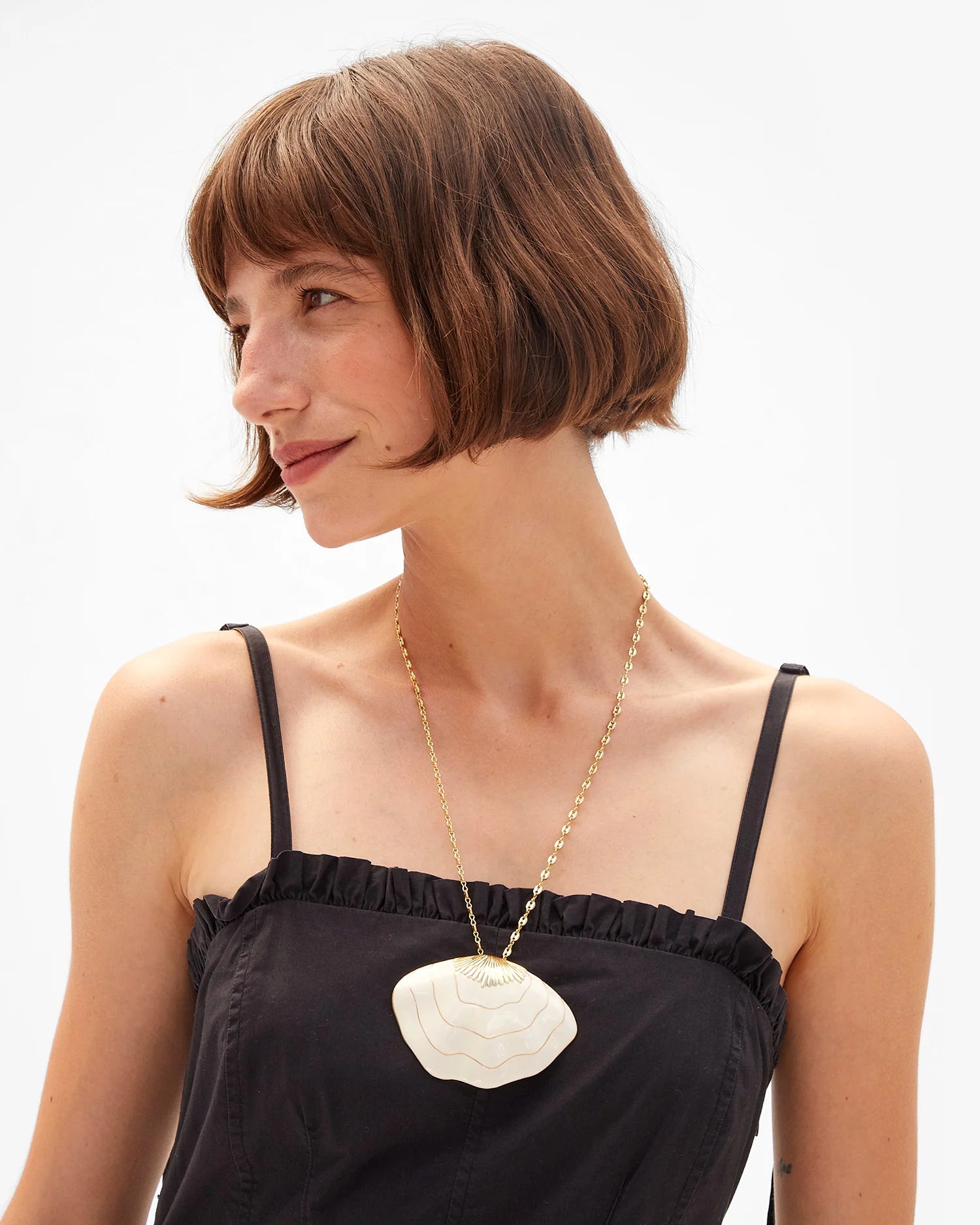 Woman wearing a black dress with a white floral pendant necklace on a white background