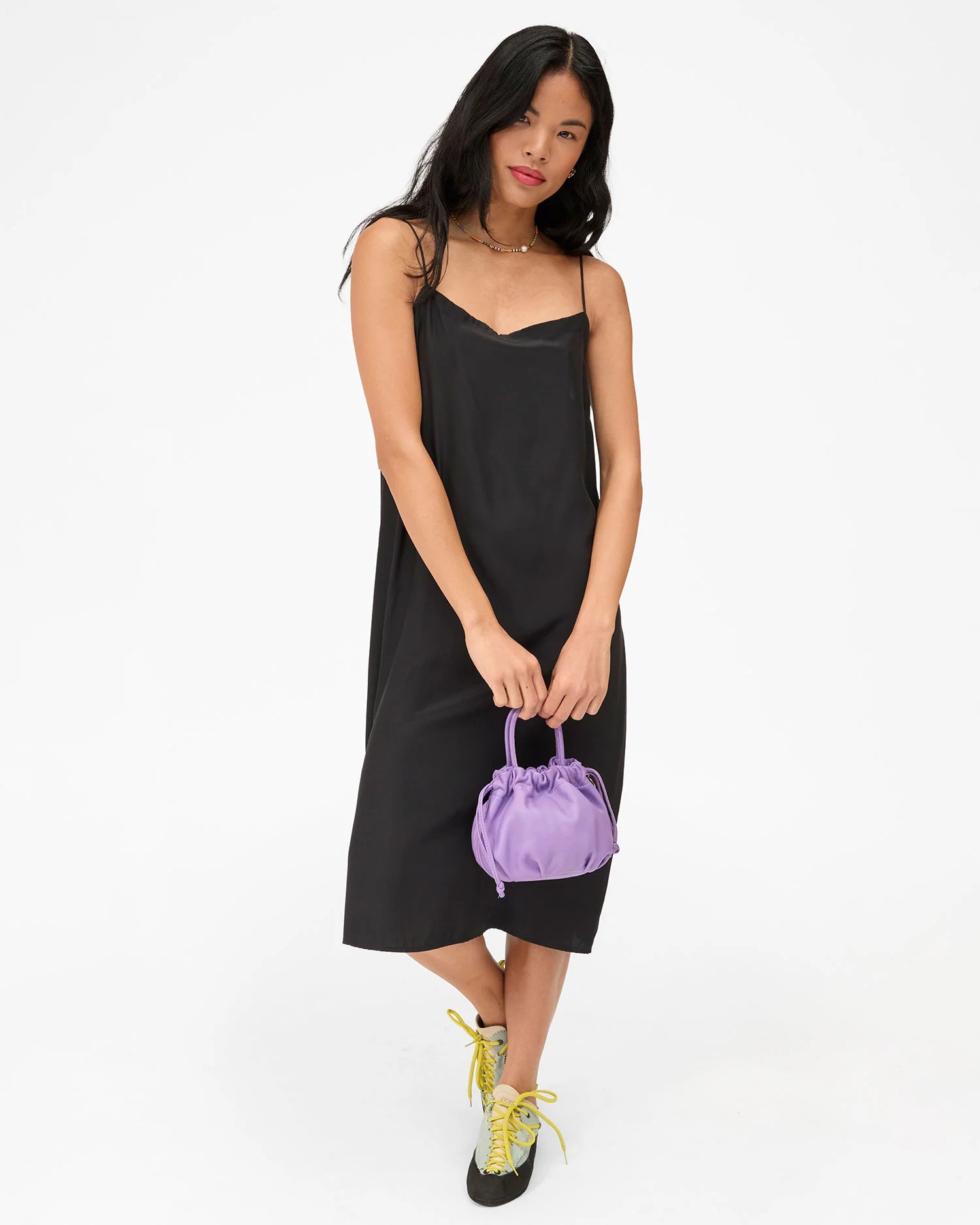 Woman holding a purple handbag wearing a black dress on a white background