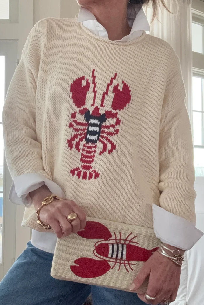 Person wearing a cream sweater with a red lobster design, holding a matching pouch.