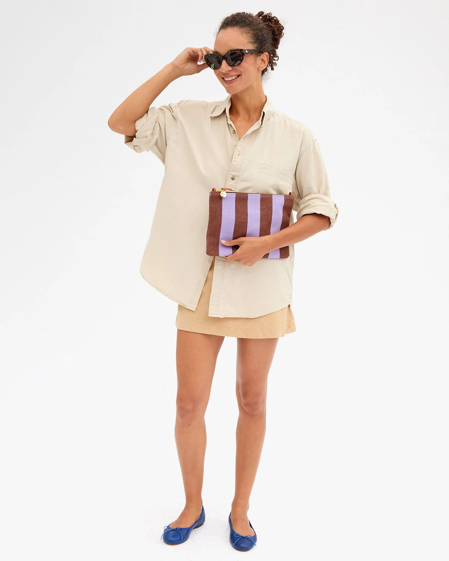Woman holding a striped clutch and wearing sunglasses on a white background