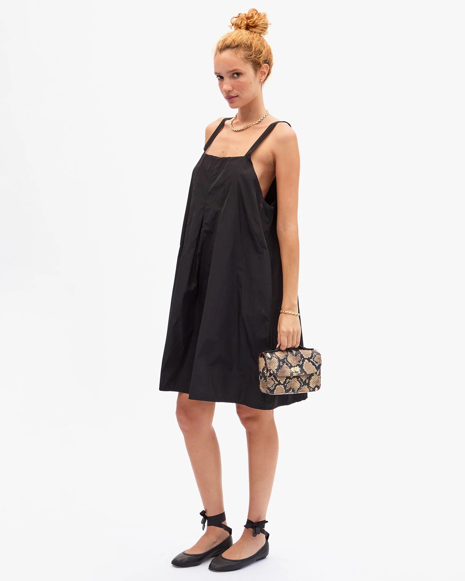 Woman wearing a black slip dress holding a patterned clutch against a white background