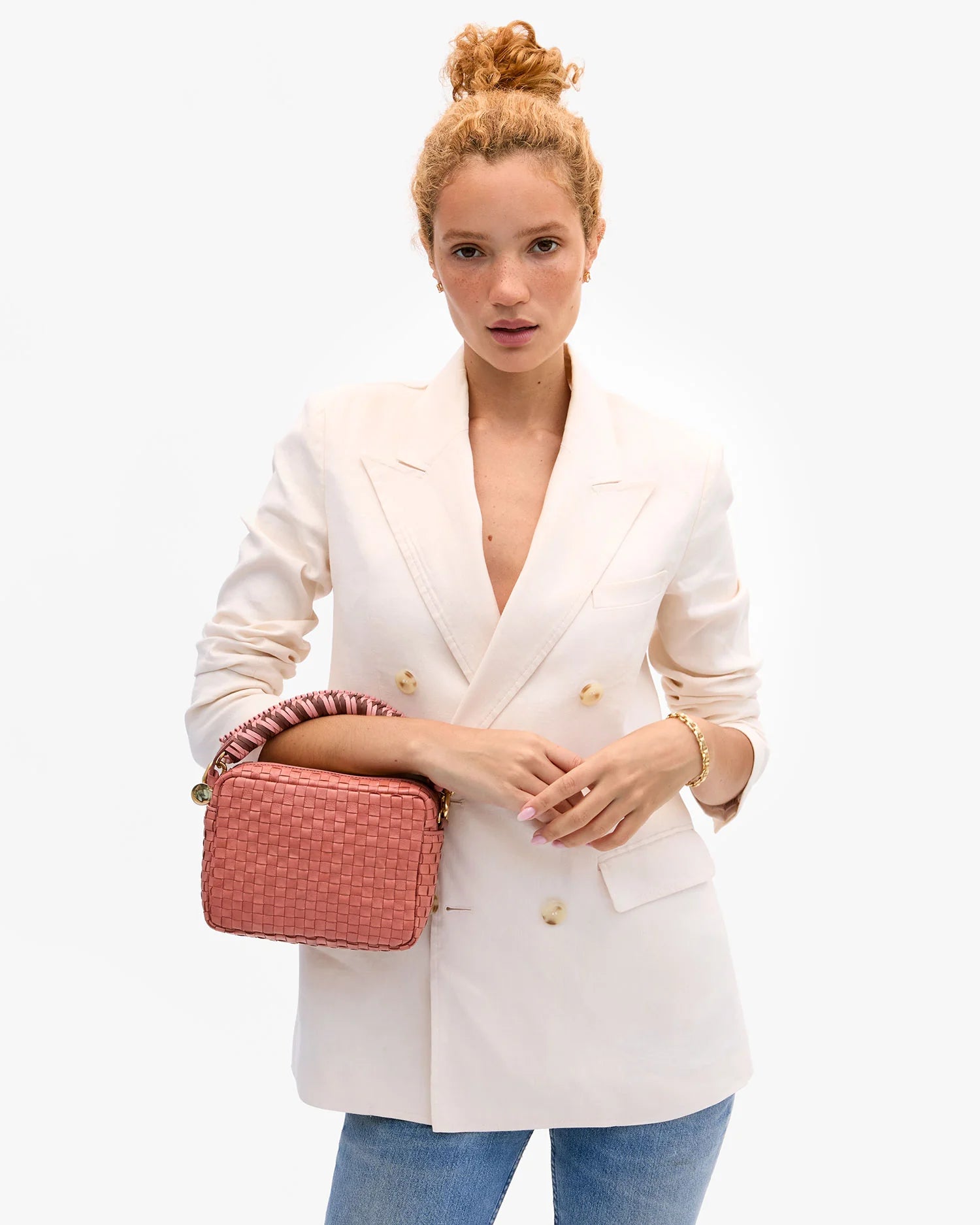 Woman wearing a white blazer holding a pink handbag on a white background
