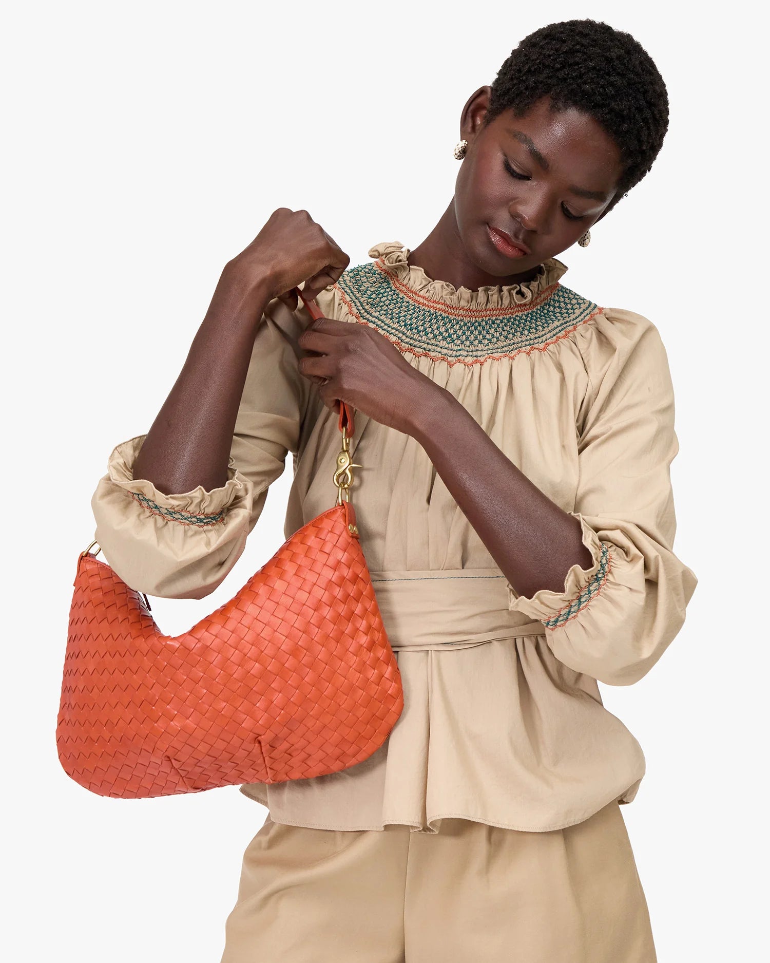 Woman holding an orange woven handbag against a white background