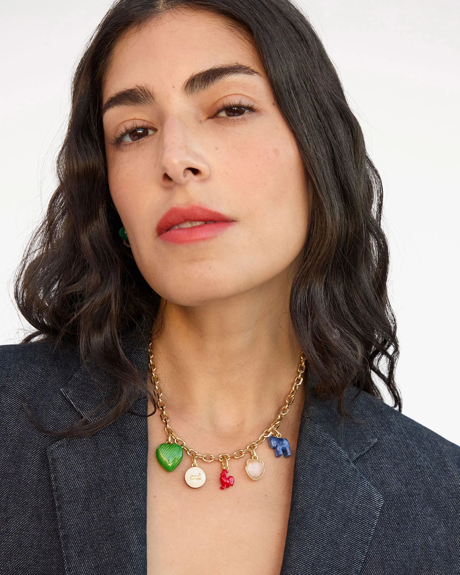 Woman wearing a gold necklace with colorful charms against a plain background