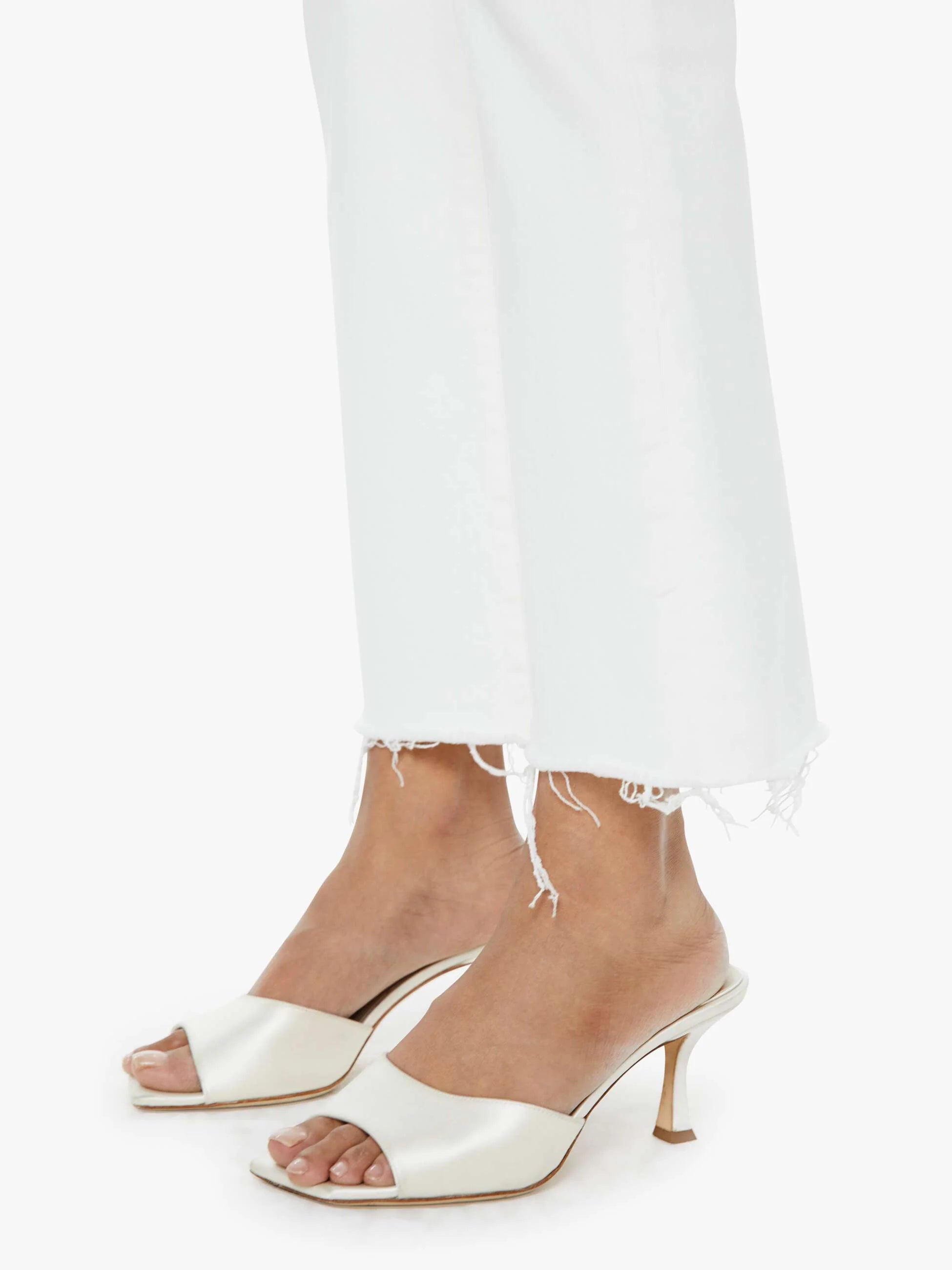 White satin high-heeled shoes worn with white pants on a white background