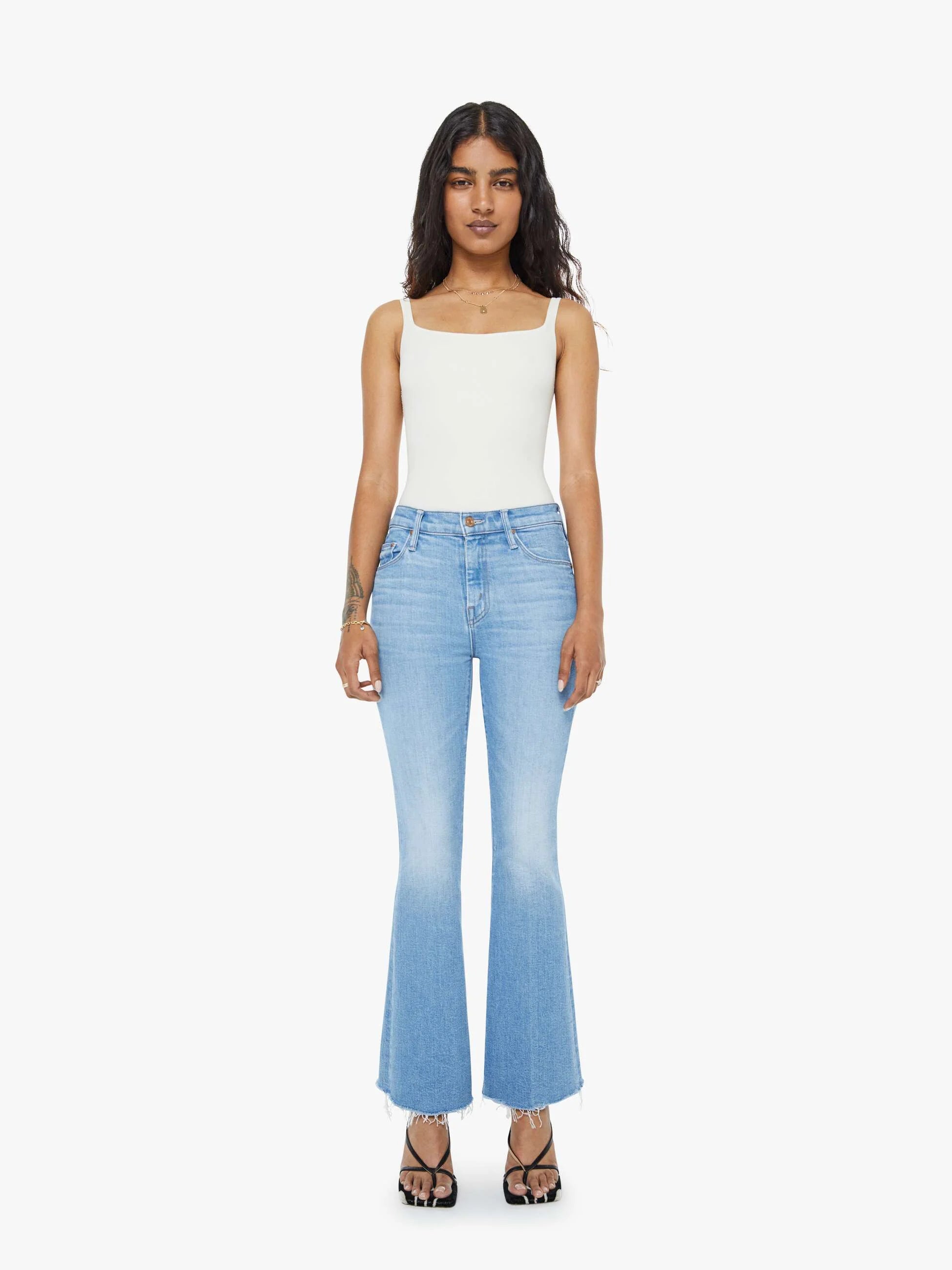 Woman wearing light blue flared jeans and a white top on a white background