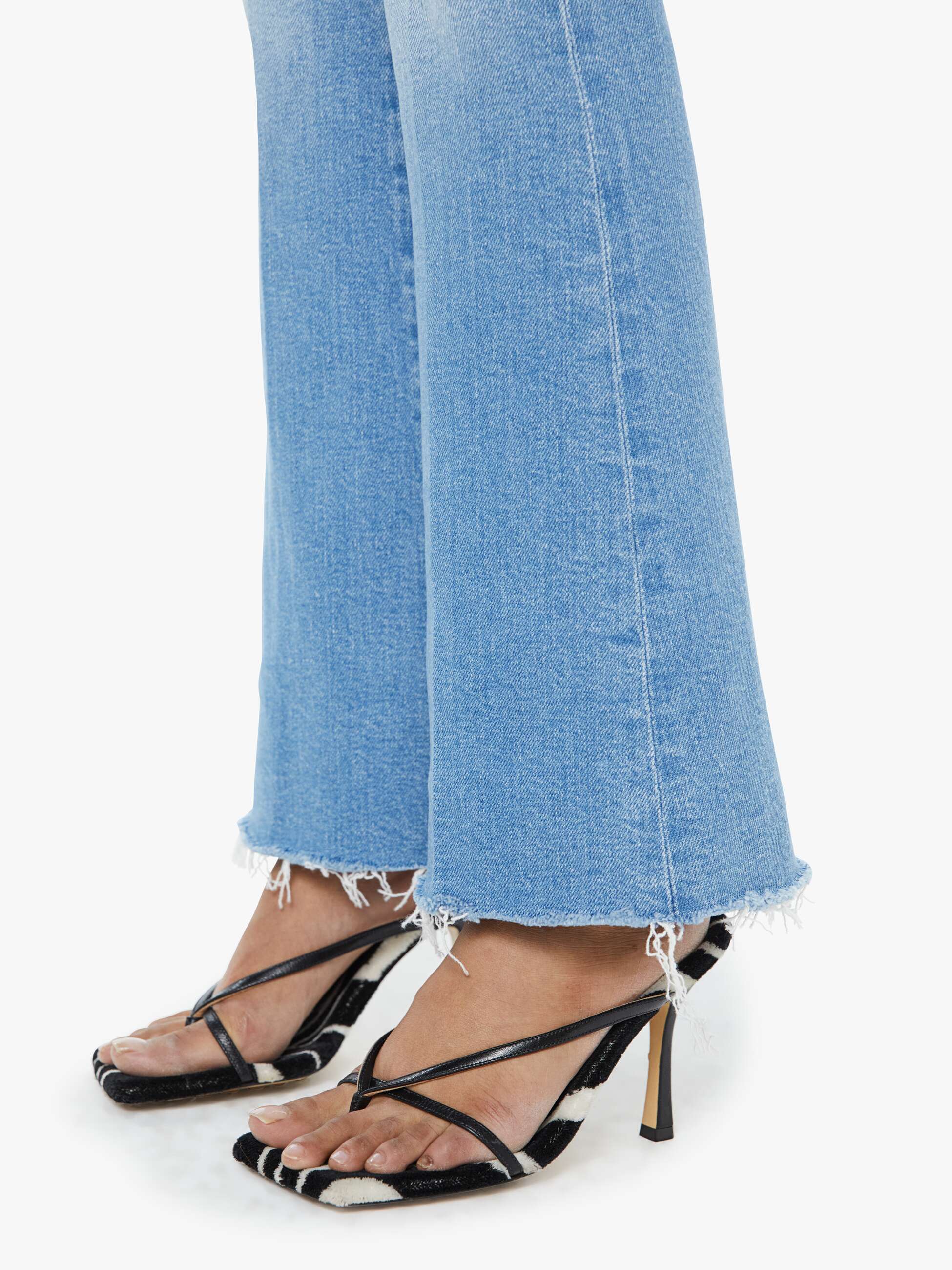 Black strappy high-heeled sandals worn with light blue jeans on a white background
